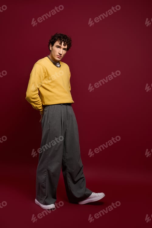 Preview: Handsome man showcases stylish outfit against rich maroon backdrop with confidence and flair