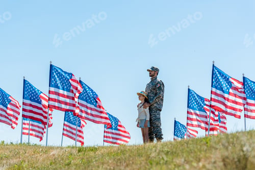 Preview: selective focus of father in military uniform standing with cute kid near american flags