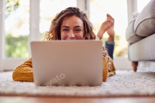 Preview: Woman In Warm Jumper Lying On Floor At Home Using Laptop