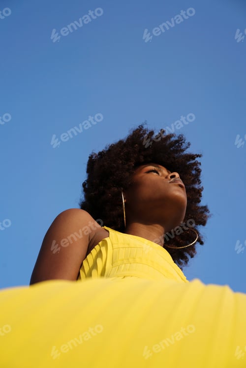 Preview: Low angle portrait of the beautiful black woman with Afro hair against blue sky