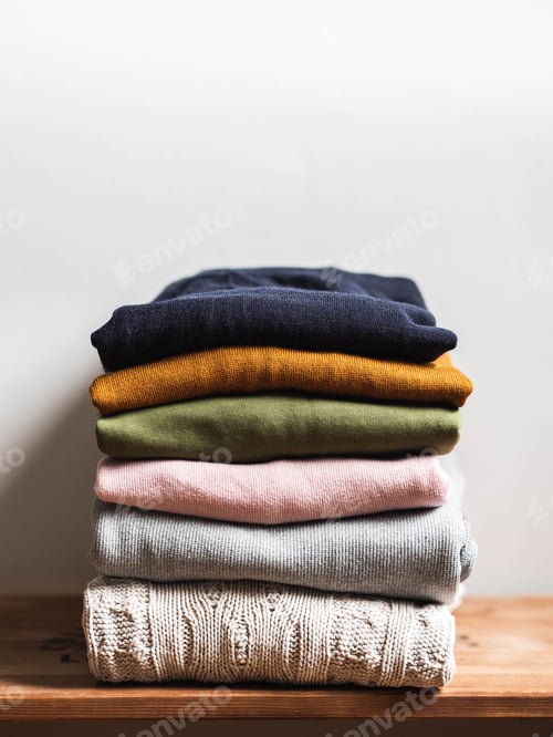 Preview: Pile of varicolored autumn clothes on wooden background, sweaters, knitwear, copy space