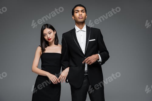 Preview: young interracial couple in elegant formal wear looking at camera isolated on grey