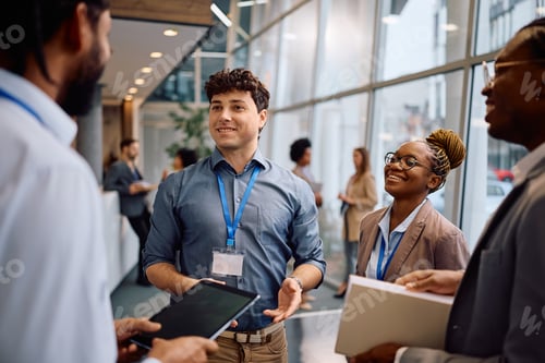 Preview: Happy businessman talking to his colleagues in hallway of a convention center.