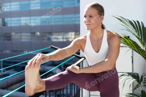 Preview: Beautiful healthy young woman doing stretching exercises in the balcony at home.