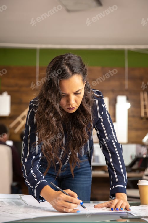 Preview: Young female architect working on blueprints in modern office