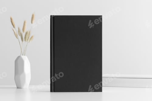 Preview: Black book mockup with a lagurus and workspace accessories on a white table.