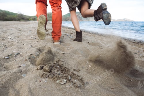 Preview: Boy and girl running together on a sandy beach, shoes and sand close-up