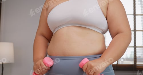 Preview: A chubby Asian woman in sportswear exercising to lose weight at home.
