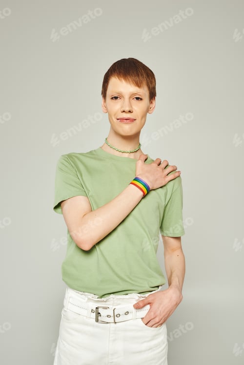 Preview: portrait of young queer person with lip gloss standing in green t-shirt and showing hand with lgbt