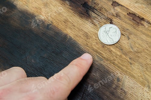 Preview: High angle closeup shop of a person pointing at a coin on a wooden surface