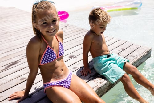 Preview: Portrait of happy biracial brother and sister sitting by the swimming pool