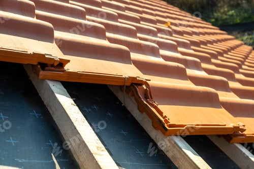 Preview: Overlapping rows of yellow ceramic roofing tiles mounted on wooden boards covering residential