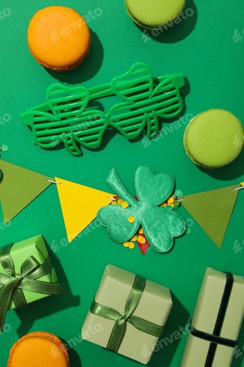 Preview: Clover leaves, paper flags, gift boxes, macaroons and glasses on green background, top view