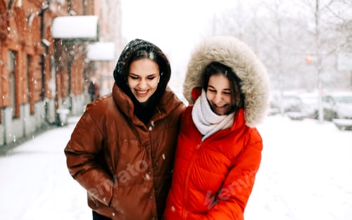 Preview: Two happy female friends enjoying snowing weather outdoors in winter during Christmas holidays