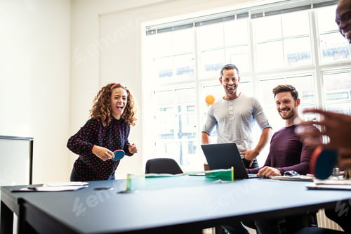 Preview: Laughing young designers playing table tennis on an office table