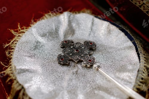Preview: Closeup of a metal, decorated cross laying on white tablecloth