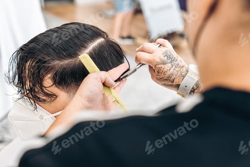 Preview: Hairdresser using scissors to cut the hair of a man with mask in a salon