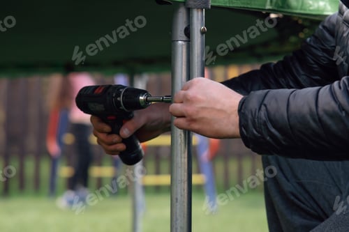Preview: Close up hands of man fastening metal frame stand to trampoline support using cordless screwdriver