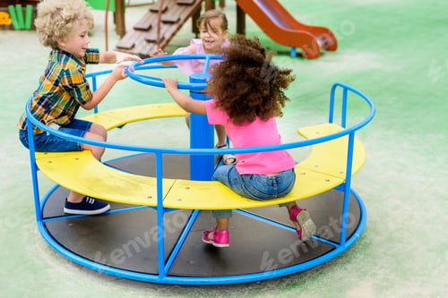 Preview: happy adorable little children riding on carousel at playground