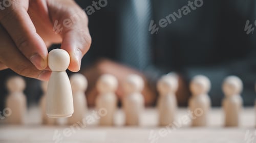 Preview: A hand holds a single wooden figure in front of a blurred background of many other figures.
