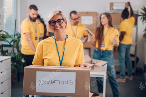 Preview: Portrait of a volunteer holding cardboard box with his colleagues in the background