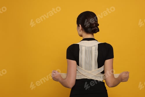 Preview: Woman with orthopedic corset on orange background, back view. Space for text