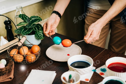 Preview: Easter day. Male Father and son painting eggs on wooden background. Family sitting in a kitchen