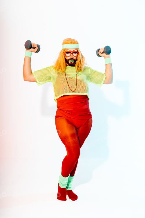Preview: Crossdressed man with beard and glasses holding two dumbells