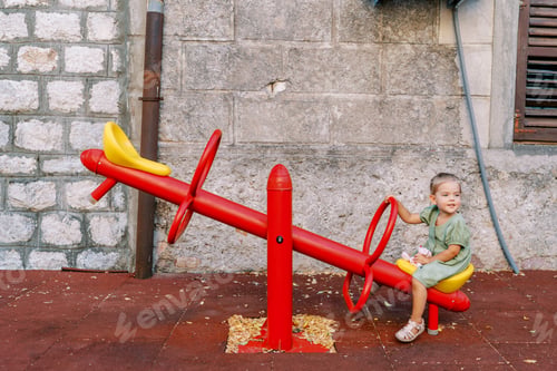 Preview: Little girl sits on a swing-balancer near an old house and looks away