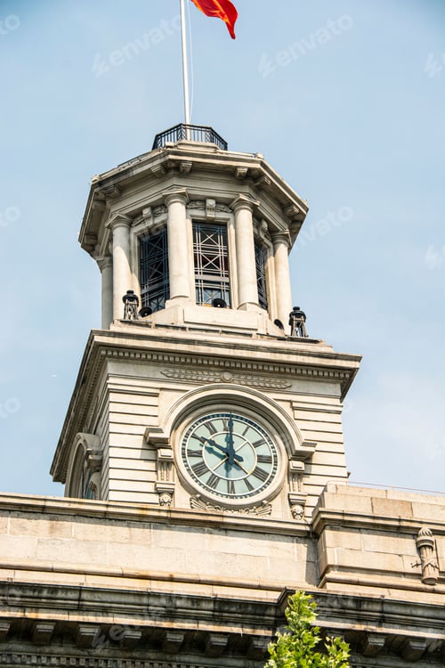 Preview: Historic clock tower with a flag on top, under a clear blue sky. Wuhan, China.