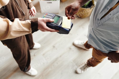 Preview: Hand of African man in casualwear paying for work of loaders while holding credit card over terminal