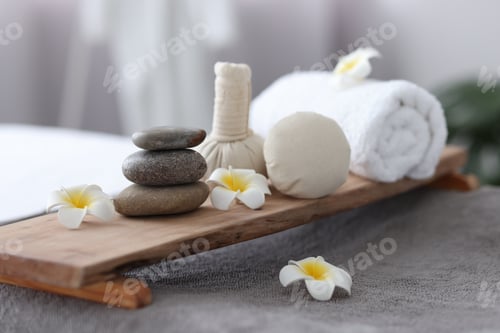 Preview: Stacked spa stones, flowers, herbal bags and towel on massage table indoors, closeup