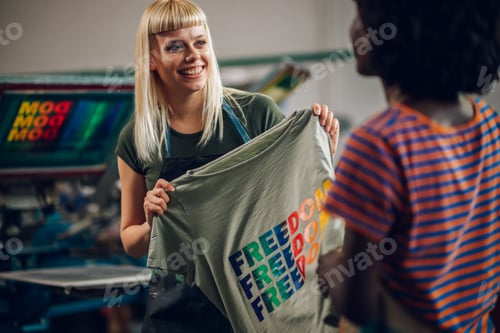 Preview: Smiling printing shop worker showing screen printed shirt to supervisor