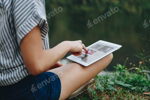 Preview: Woman alone in nature using a digital tablet with entertainment application on the screen