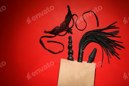 Preview: Paper shopping bag with different sex toys on red background, flat lay