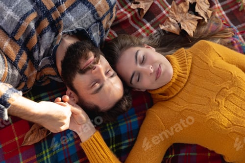 Preview: Overhead view of smiling caucasian couple lying on rug in garden holding hands with eyes closed