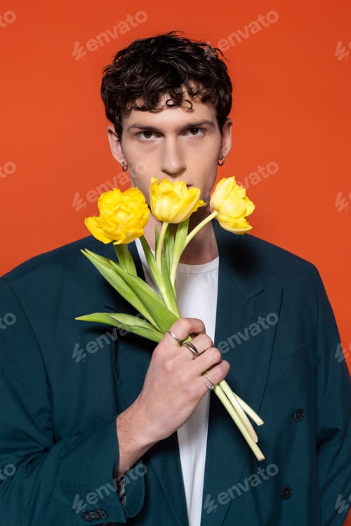 Preview: Trendy brunette man in blue blazer holding yellow tulips isolated on red