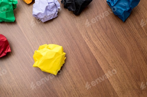 Preview: yellow crumpled paper ball on dark brown wood table with group of colorful crumpled paper