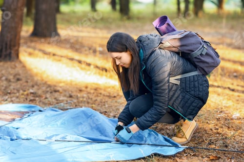 Preview: Young woman setting tent in camp, backpacking at countryside
