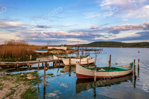 Preview: The tranquil afternoon on a lake with a wooden pier and boats in the colorful sky.