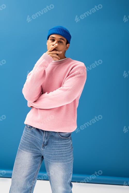Preview: Handsome young man shows off stylish pink sweater and blue beanie in vibrant setting
