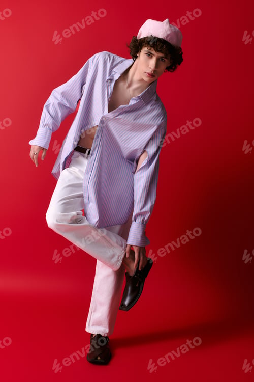 Preview: Stylish young man striking a pose against vibrant red backdrop in fashionable attire