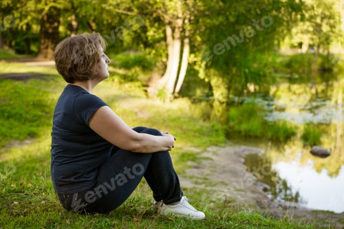 Preview: Adult woman sitting in the park on the grass in the rays of sunset Sunny