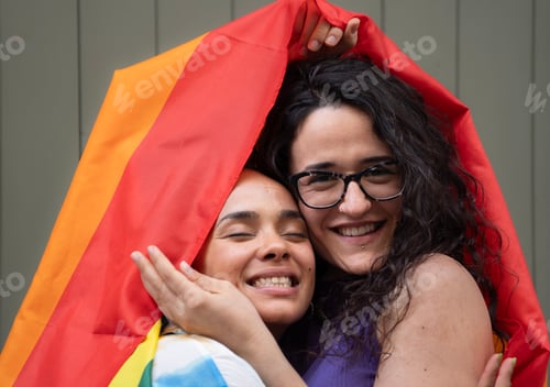 Preview: Two women couple are hugging and caressing under a rainbow flag with happy expression
