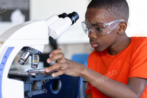 Preview: Using microscope, boy in safety goggles studying science in school laboratory
