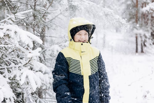 Preview: Winter portrait of happy teenager boy looking snow falling down in forest Child having fun outdoors
