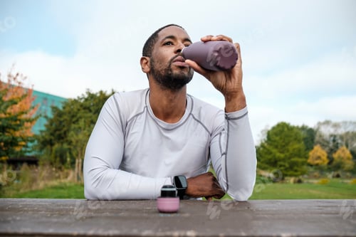 Preview: Athletic man drinking water from reusable bottle after workout in park