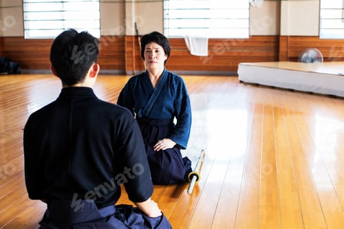 Preview: Female and male Japanese Kendo fighters kneeling opposite each other on wooden floor.