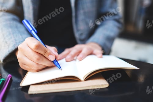 Preview: Closeup image of a woman writing on a blank notebook with colored pens on the table
