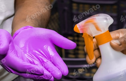 Preview: Man spraying hand sanitizer on hands wearing purple glove